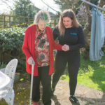 physiotherapist and elderly lady walking with a walking stick outdoors