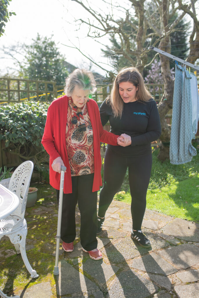 physiotherapist and elderly lady walking with a walking stick outdoors
